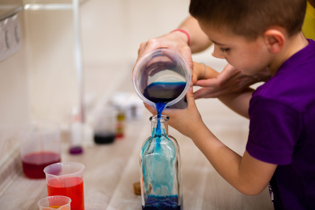 4-year-old boy adding colored water in a glass bottle for a scie